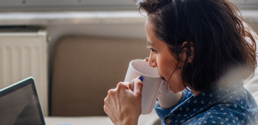 a woman sipping on coffee looking at her laptop